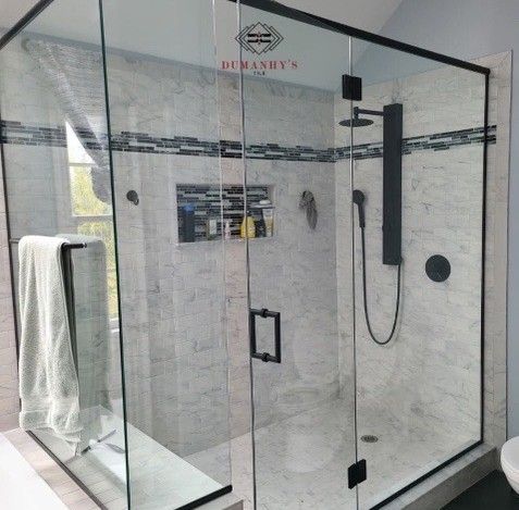Modern shower with clear glass enclosure and black fixtures, marble tiles, and built-in bench.
