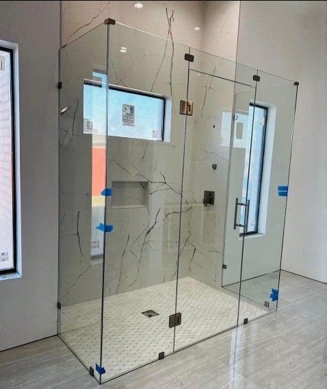 Glass shower enclosure with marble-like tile walls, door, and a small window.