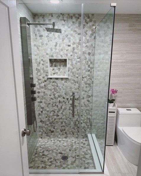 Modern bathroom with a glass shower, pebble tile, and a built-in shelf.
