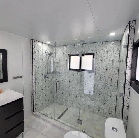 Modern bathroom with glass shower, patterned tile, dark vanity, and toilet.