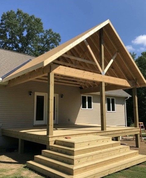 Newly built wooden porch with steps, attached to a light-colored house, under a blue sky.