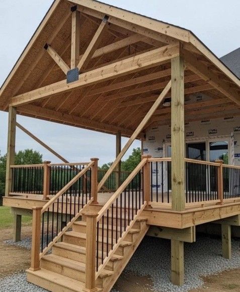 Wooden deck and porch addition to a house with black metal railings, stairs, and exposed wooden beams.