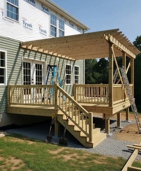 Newly built wooden deck with stairs and pergola attached to a house with light green siding.