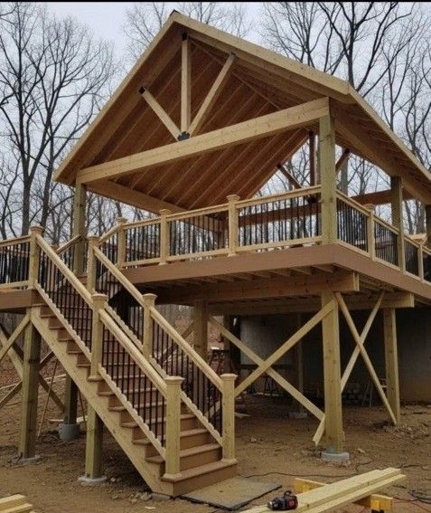 Wooden elevated deck with stairs and roofed structure. Railings are black. Exterior shot.