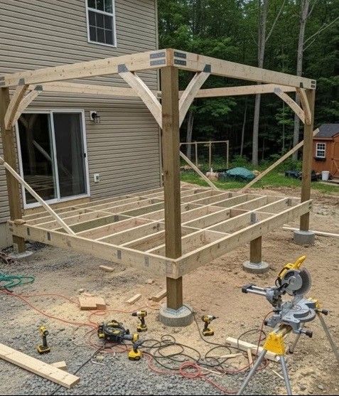 Deck frame construction. Wooden beams and posts, tools, and a sliding glass door are visible outdoors.
