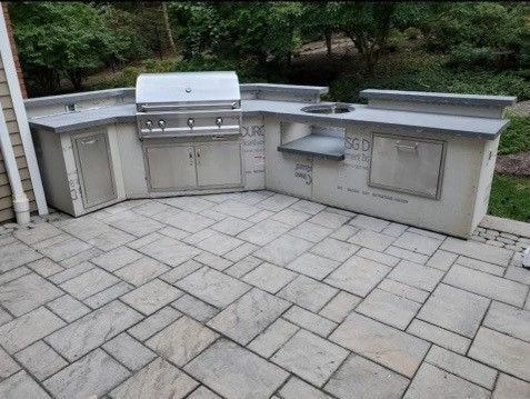 Outdoor kitchen with built-in grill, sink, and cabinets on a stone patio.