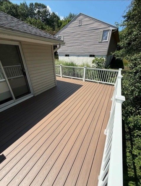 Composite deck with white railing next to a house with beige siding and a dark roof.
