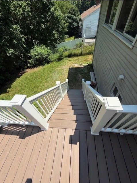 Wooden deck and stairs leading down to a grassy area, flanked by white railings and a house.