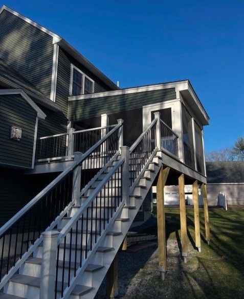 Exterior view of a house with an attached screened porch. Staircase leads up to the porch. Green siding, blue sky.