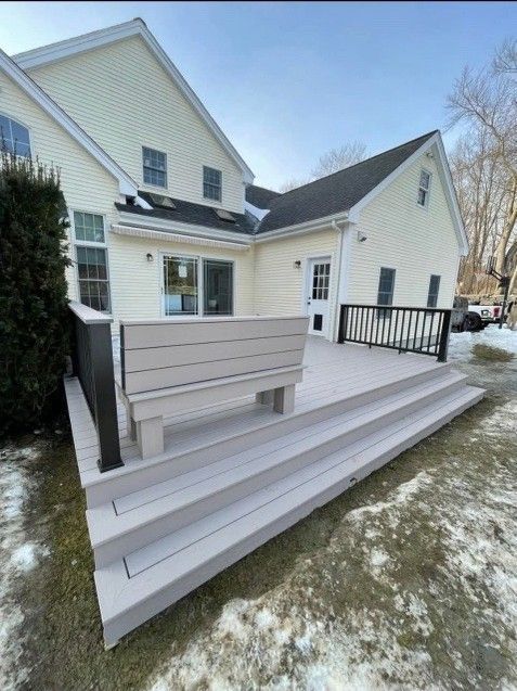 Light gray deck with steps and planter box attached to a pale yellow house, snow on the ground.