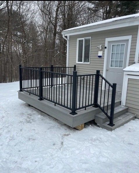 A snow-covered deck with black railings and steps next to a light-colored building with a door and window.