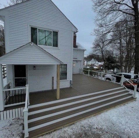 Back of a white house with a deck and steps, covered in snow.