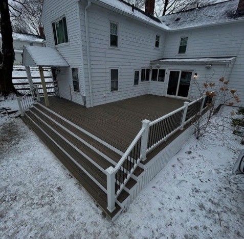 White two-story house with a large deck and stairs covered in snow.