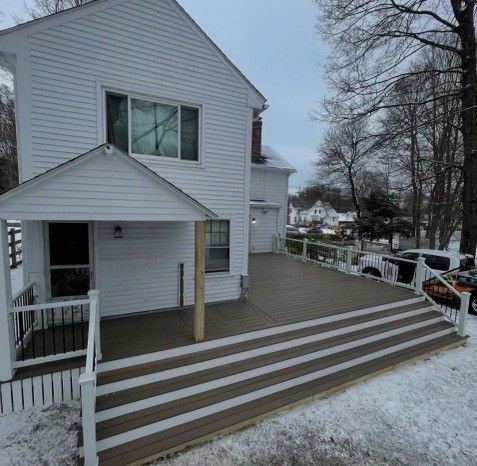 White house with large deck and steps, covered in snow, on a cloudy day.