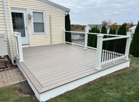 Tan composite deck with white railing, next to a yellow house with a lawn.