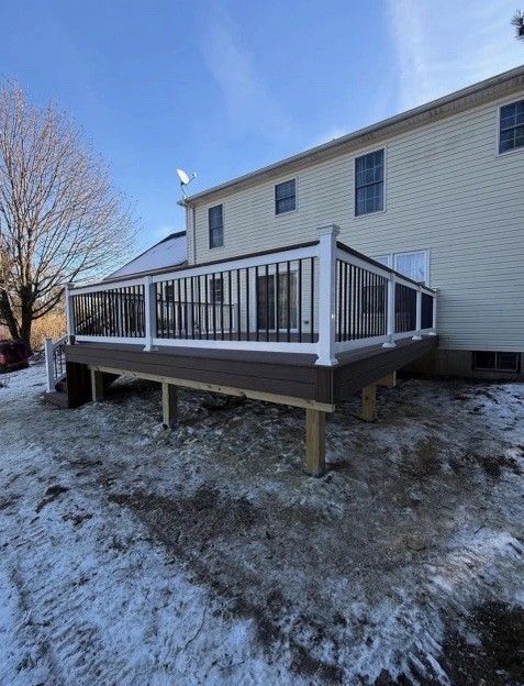 Brown deck with white and black railing attached to a beige house, snow on the ground.