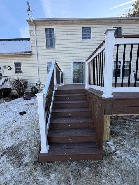 Deck with brown steps and railing, white posts, leading to a sliding glass door. Snow covers the ground.