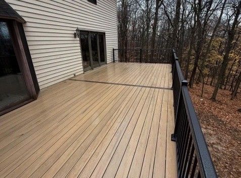 Wooden deck with black railings and a house in the background, surrounded by trees.
