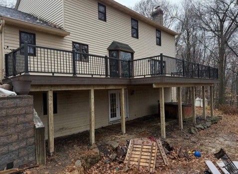 Two-story house with a wooden deck. Black railings. Brown siding. Beige house with several windows.