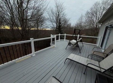 Gray deck with white railing, chairs, and a swing outdoors.