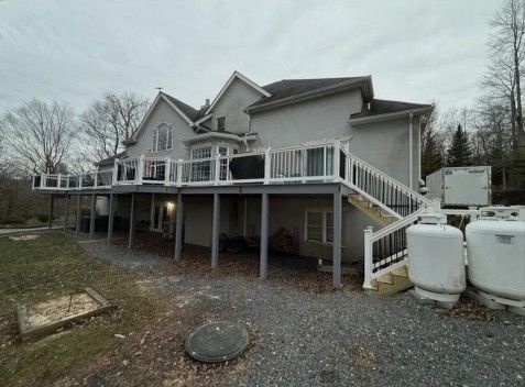 Two-story house with a large deck, white railings, and several propane tanks in the yard.