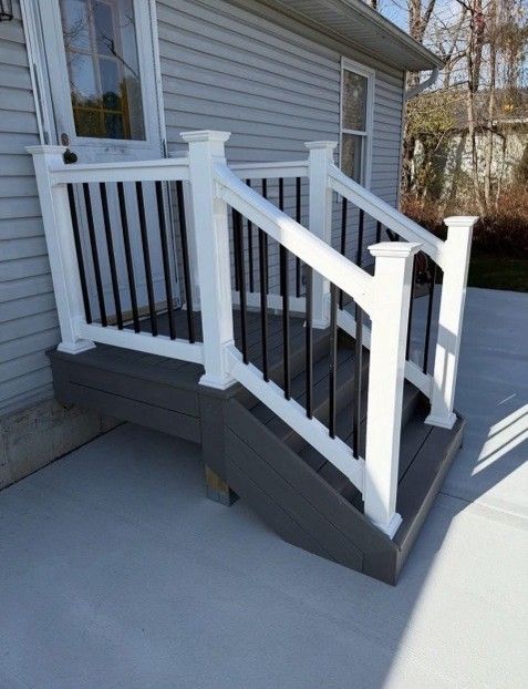 Gray composite deck with white railing and black balusters. Doorway in the background.