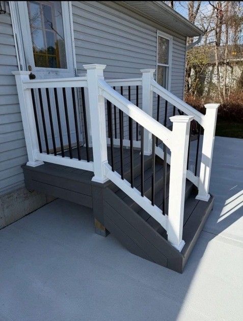Gray composite steps and deck with white railing, black spindles, and a door to the house.