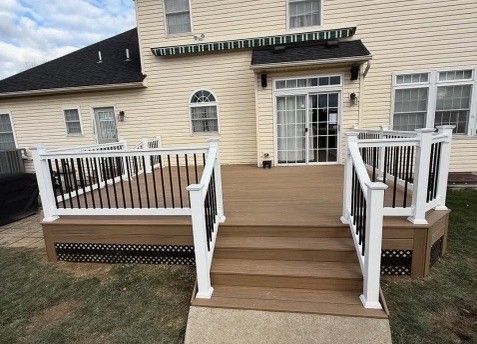 A backyard composite deck with white railings and black balusters. A sliding glass door leads to a light yellow house.