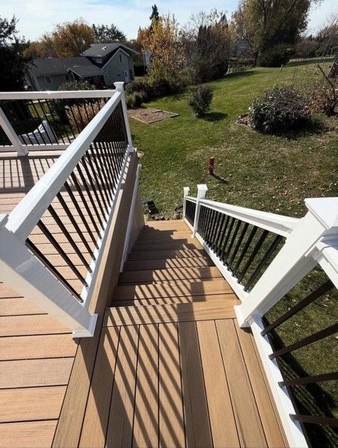Wooden deck with stairs leading down to a grassy yard, black railing spindles and white posts.