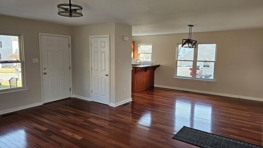 An interior of a home with hardwood floors, neutral walls, and a view of the kitchen area.