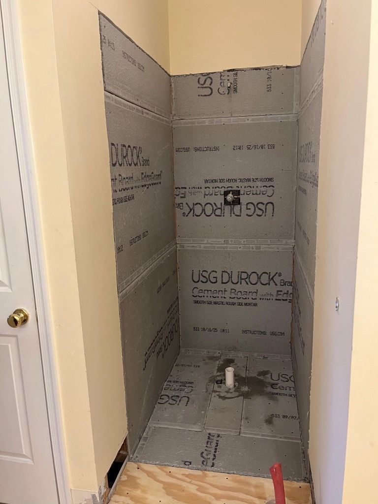 Shower stall in construction phase, with cement board walls and floor, set in a room with yellow walls.