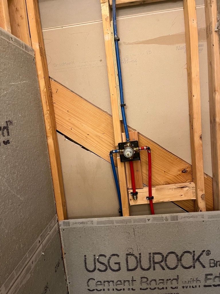 Plumbing rough-in with blue and red pipes in a wooden framed wall. Cement board is installed on lower portion.