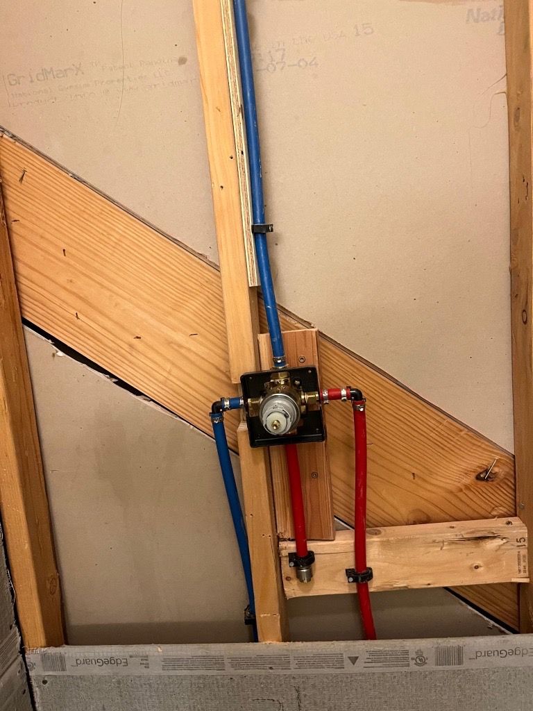 Piping for a shower valve, blue and red pipes, mounted on wood framing within a wall.