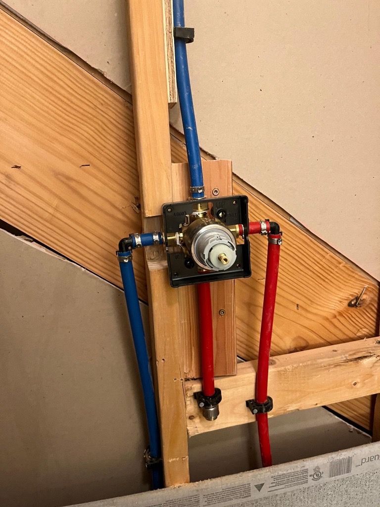 Plumbing rough-in: PEX water pipes connected to a shower valve mounted on wooden studs.