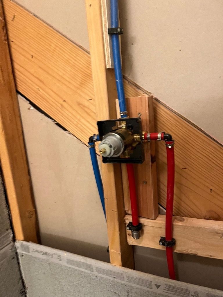 Shower valve plumbing installation with red and blue pipes attached to a valve in a wooden frame.