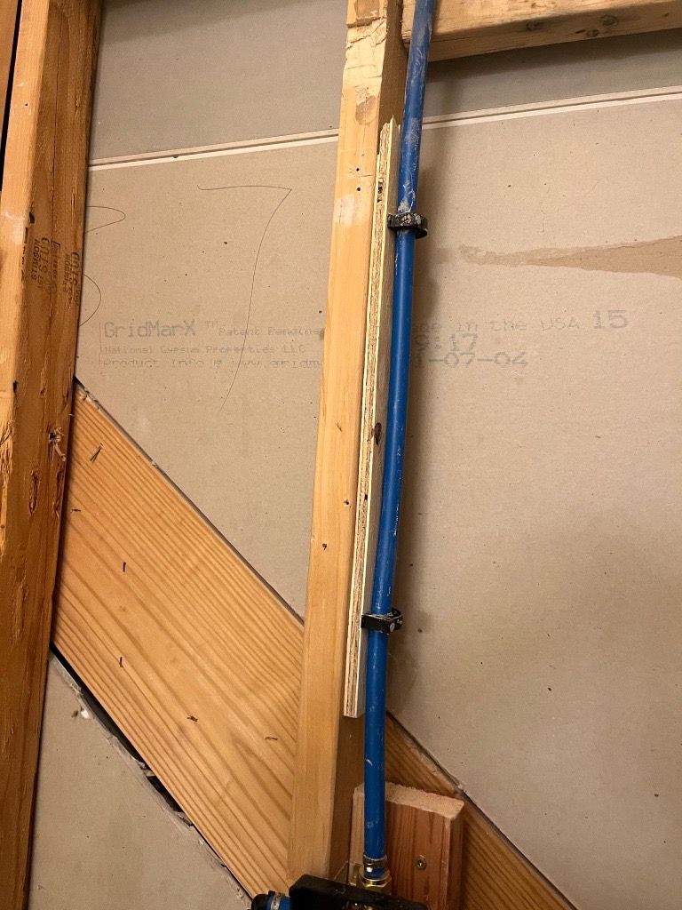 Blue water pipe secured to a wooden frame with black clips. Construction scene with drywall background.