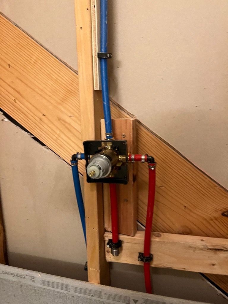 Shower valve installation with blue and red PEX pipes, mounted on wood framing, against a wall.