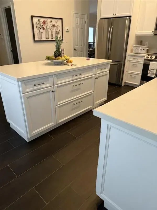 White kitchen island with countertop, drawers, and cabinet doors. Dark brown tile floor.