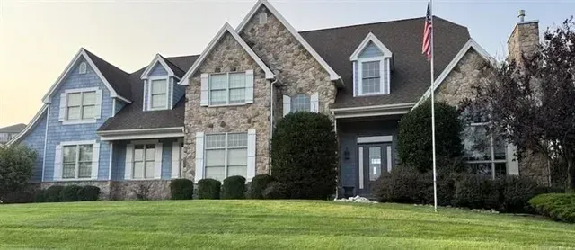 Large house with blue and stone exterior, American flag, green lawn.