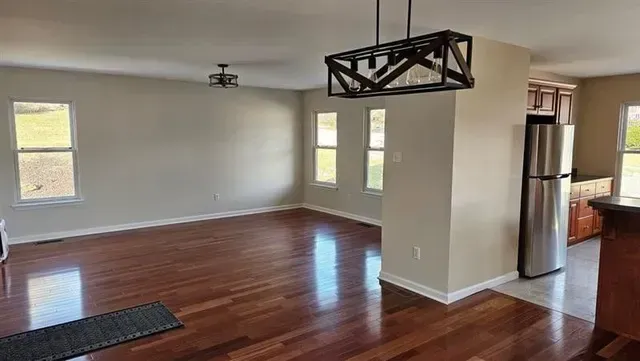 Empty living room with wood floors, neutral walls, and a modern chandelier.