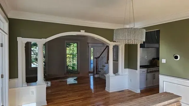 Interior view of a room with green walls, white trim, hardwood floors, and a crystal chandelier.