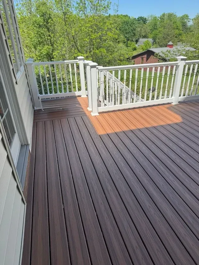 Deck with dark brown composite boards, white railing, and a view of trees and a building.