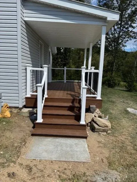 A small, wooden porch with white railings and steps leads to a house with gray siding.