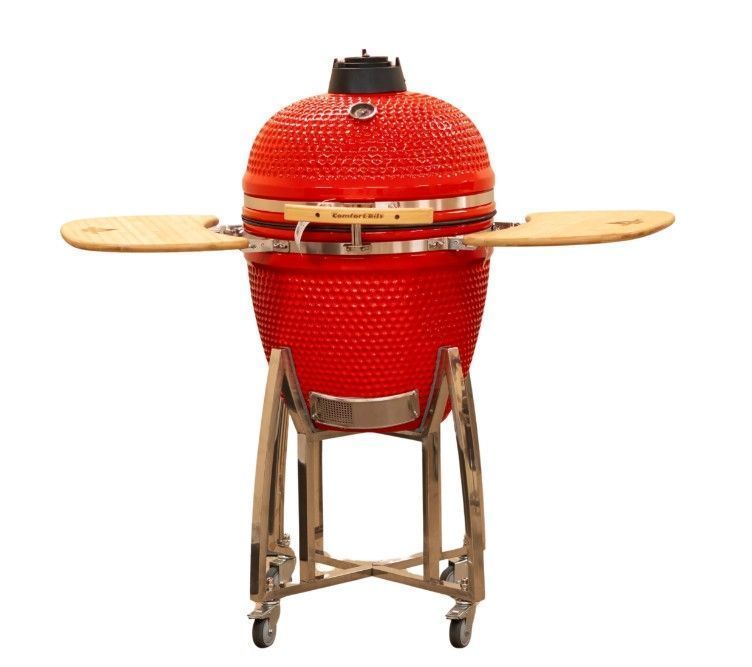 Red ceramic barbecue grill with wooden side shelves on a metal stand, isolated on white background