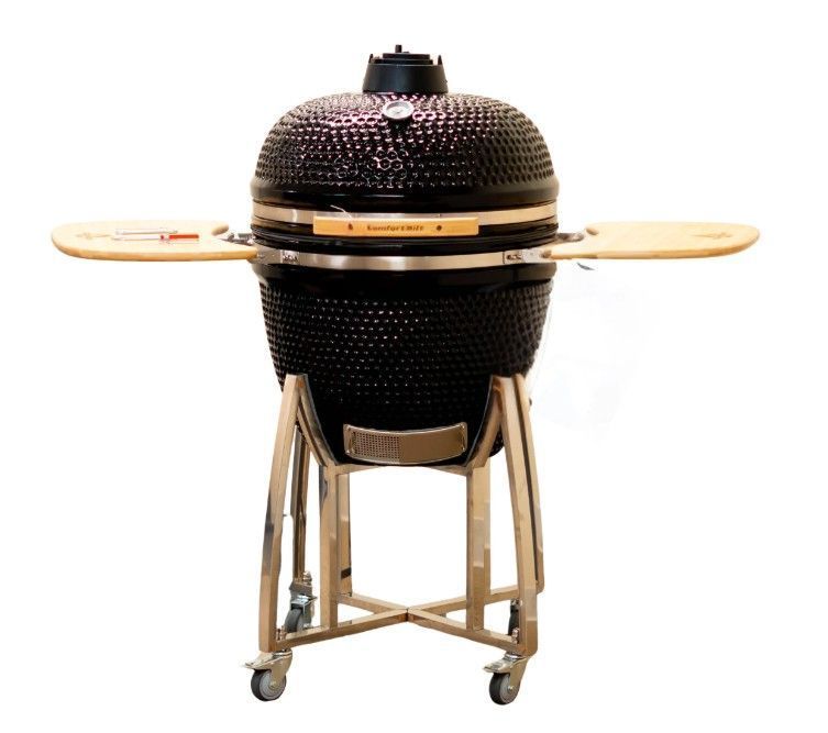 Black ceramic kamado grill on a wheeled wooden stand, with side shelves and vent top