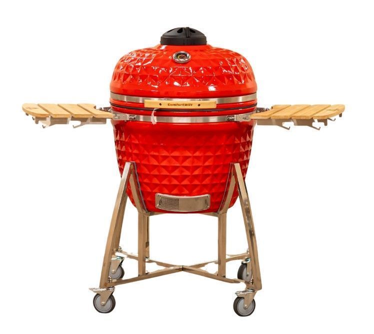 Red ceramic kamado grill on a wheeled wooden stand with side shelves.