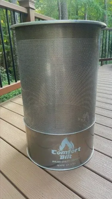 Gray mesh cylindrical trash can on a wooden deck with a black railing and green foliage in the background