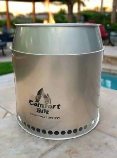 Silver metal outdoor fire pit with “Comfort Bill” logo on a patio near a pool