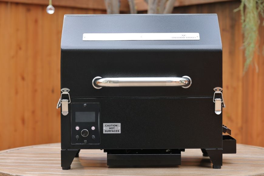 Black outdoor pizza oven on a wooden table against a wood-paneled wall