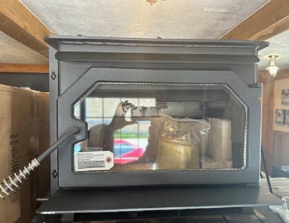 Black wood-burning stove with glass door and brass accents inside a room, showing reflections on the glass.